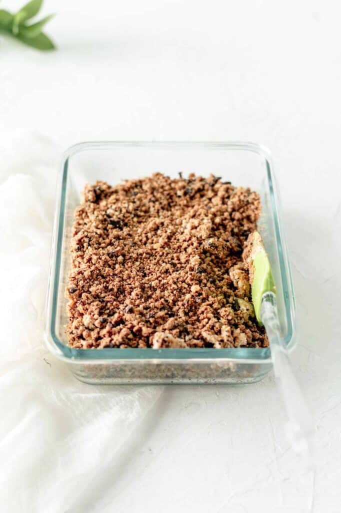 Pressed keto cookie dough layer set in a glass dish, forming the base for the crumbly cookie dough bars.