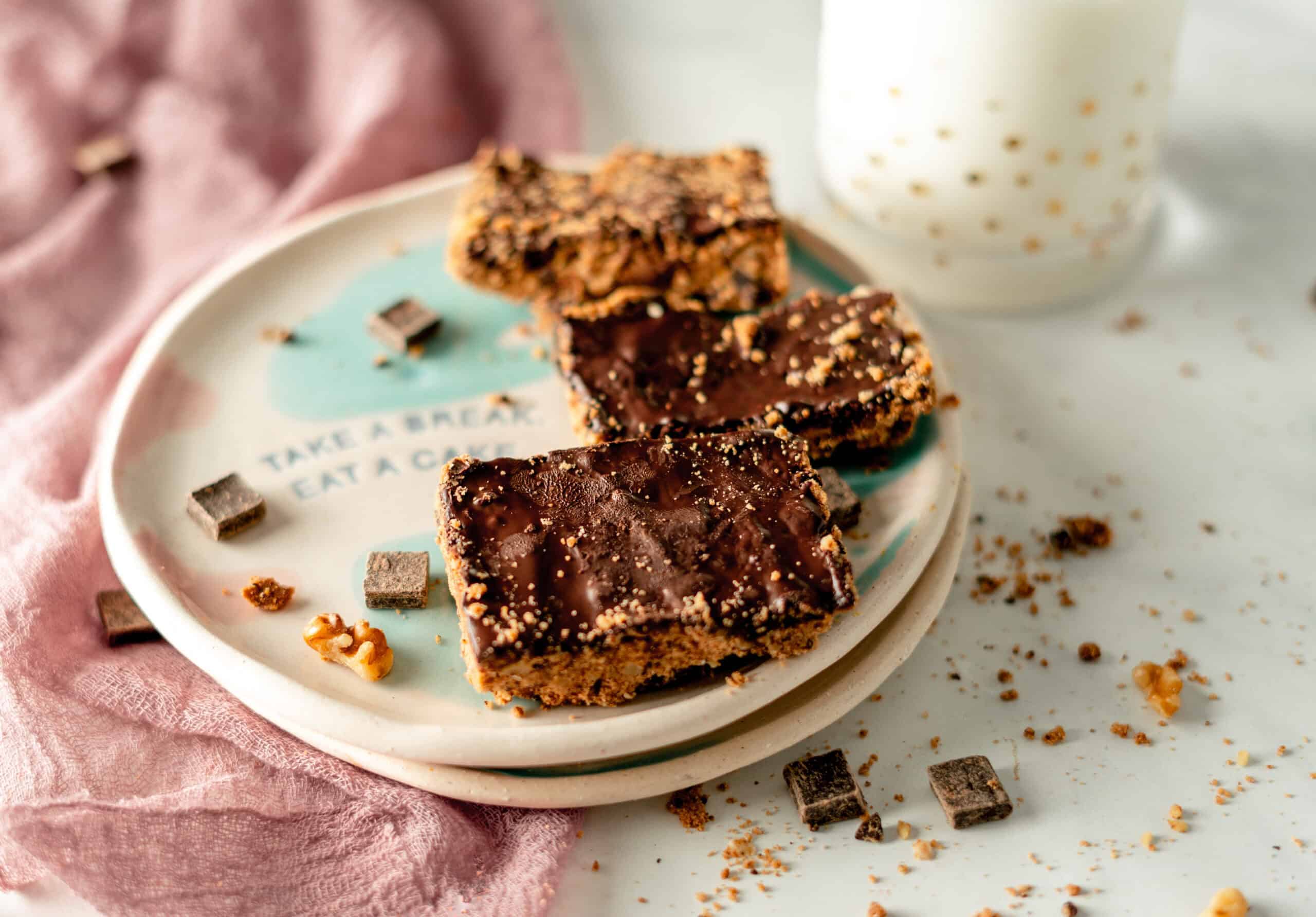 Keto crumbly cookie dough bars topped with rich chocolate, served on a plate with scattered chocolate chunks and walnuts.