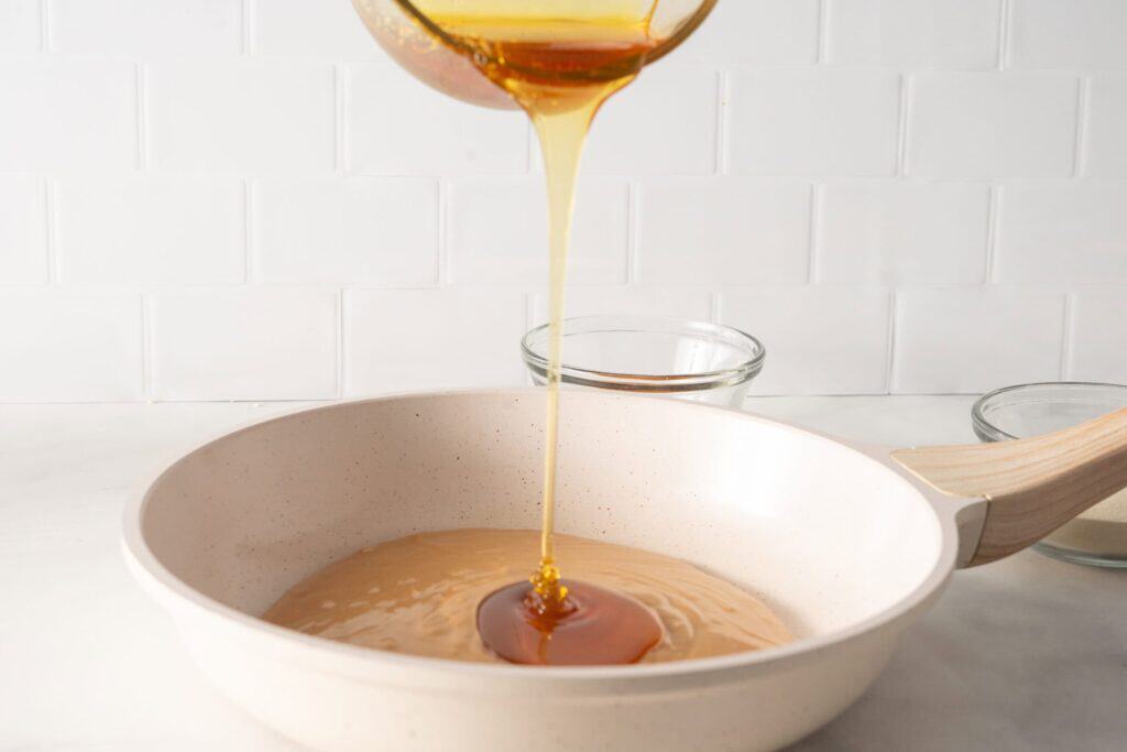 Honey is being poured in the mixture of peanut butter into a pan.