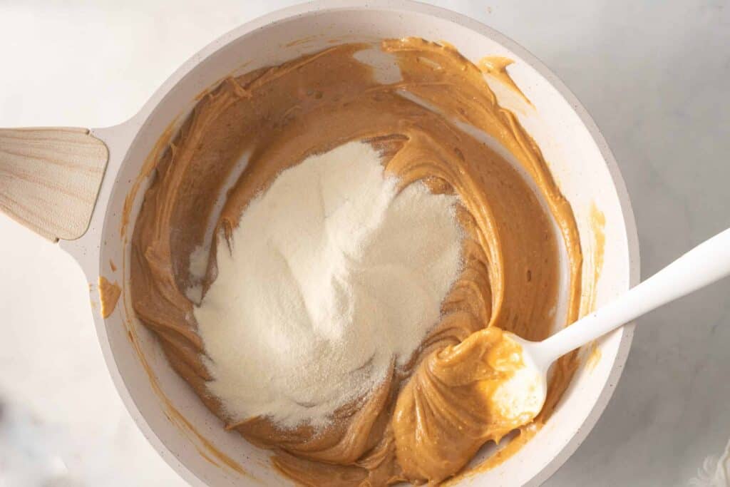 A mound of white powder has just been added to peanut butter mixture in a pan.