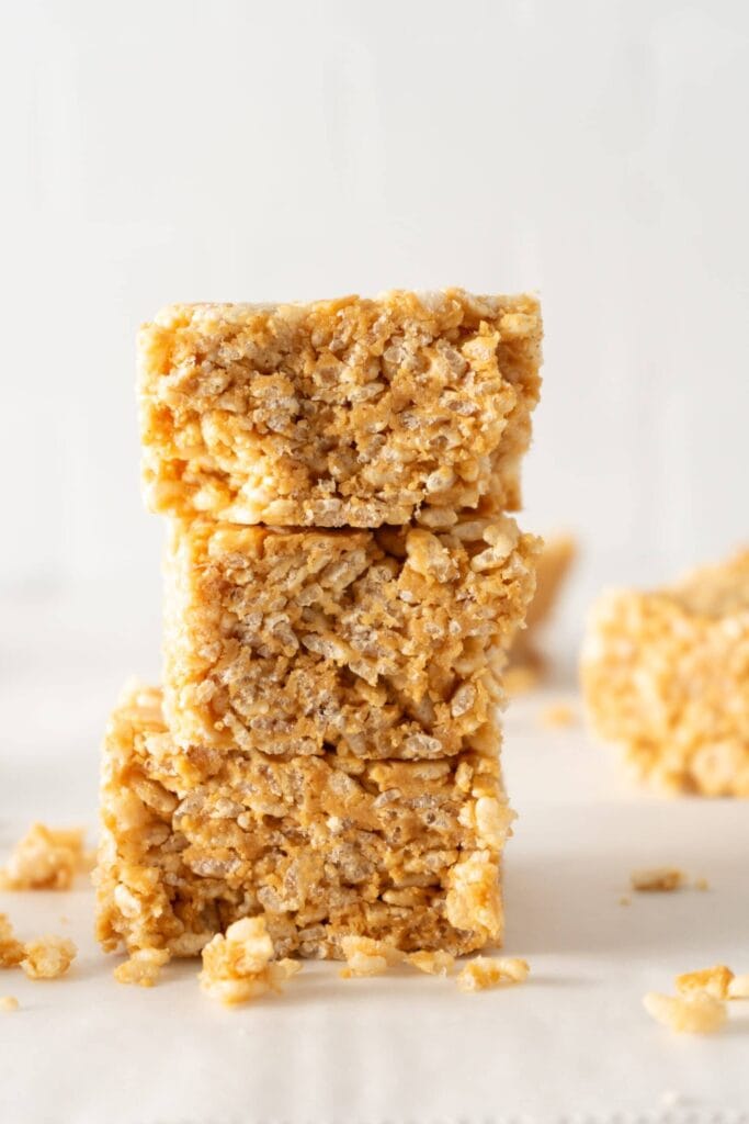 Close-up of three stacked Rice Krispie Treats showing their crispy texture and golden color, with some crumbs around.