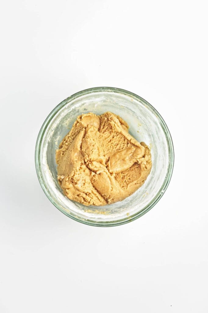 Overhead view of a small glass jar filled with peanut butter cookie dough on a white background.