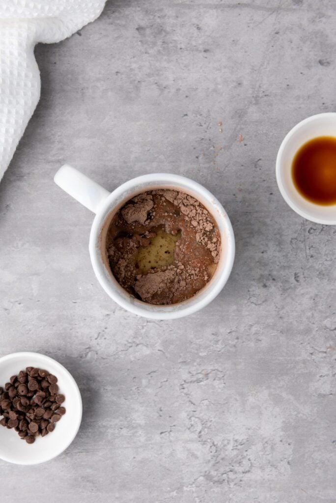 Mug with brownie batter partially mixed, with dry cocoa powder still visible on top.