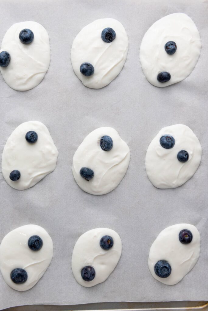 Small dollops of yogurt topped with fresh blueberries, evenly spaced on parchment paper.