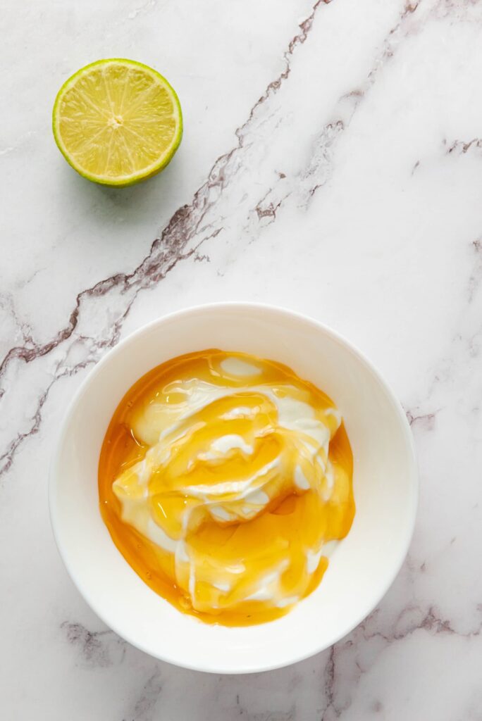 Bowl of yogurt drizzled with honey on a white marble surface.