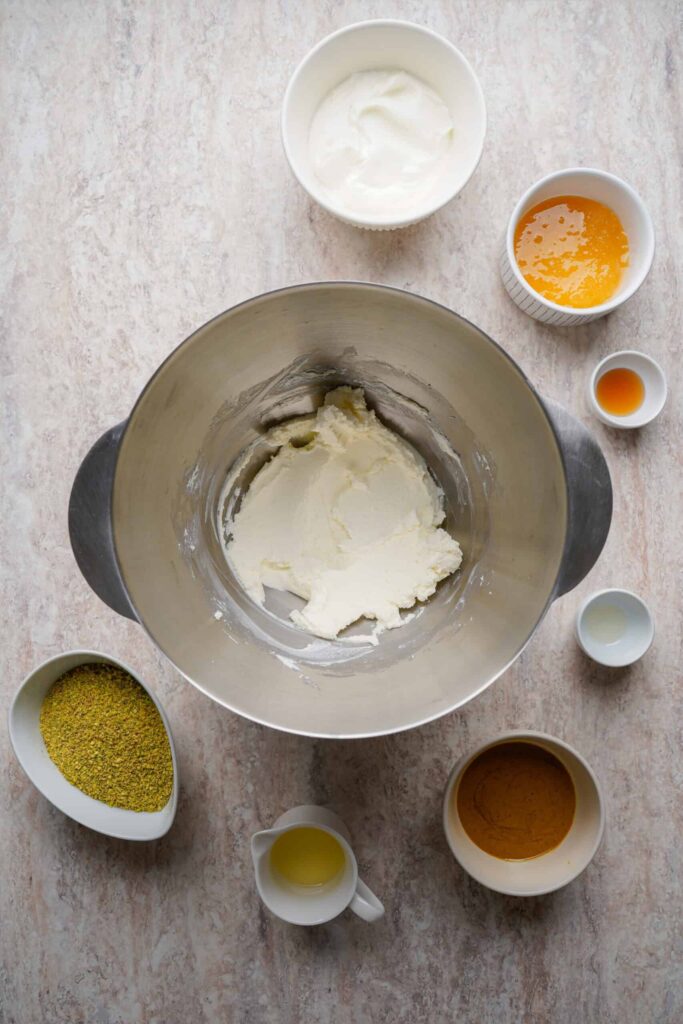 Whipped cream cheese in a mixing bowl with other ingredients placed alongside on the counter.