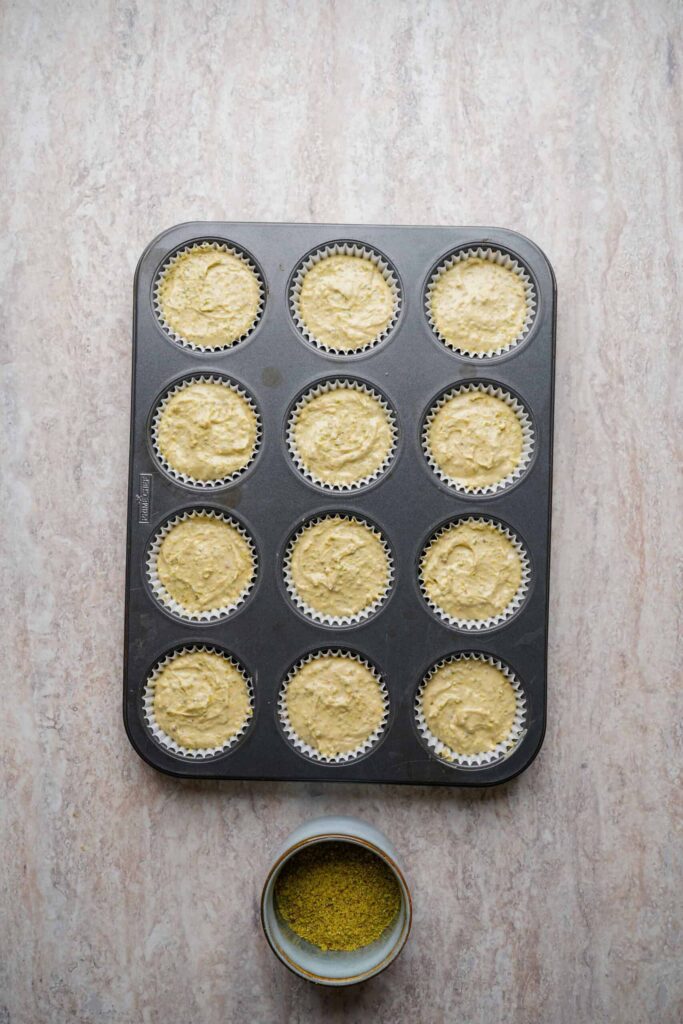 Mini cheesecake batter portioned evenly into lined muffin cups in a baking tray, ready to bake.