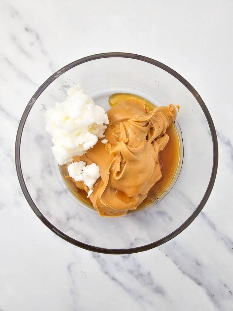 Peanut butter, coconut oil, and maple syrup combined in a bowl before mixing.