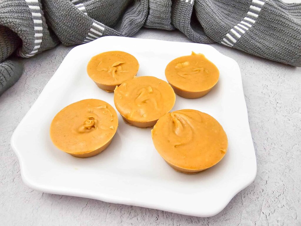 Healthy salted peanut butter fudge pieces on a white plate, smooth and creamy with a glossy finish.