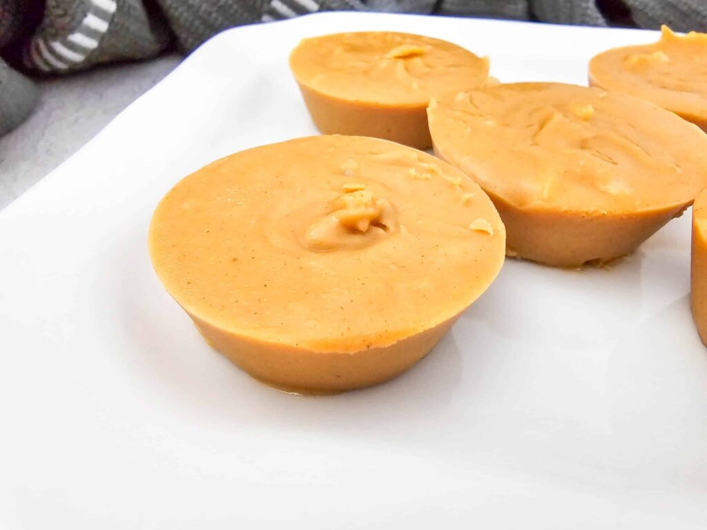 close up view of peanut butter fudge pieces on a white plate, smooth and creamy with a glossy finish.