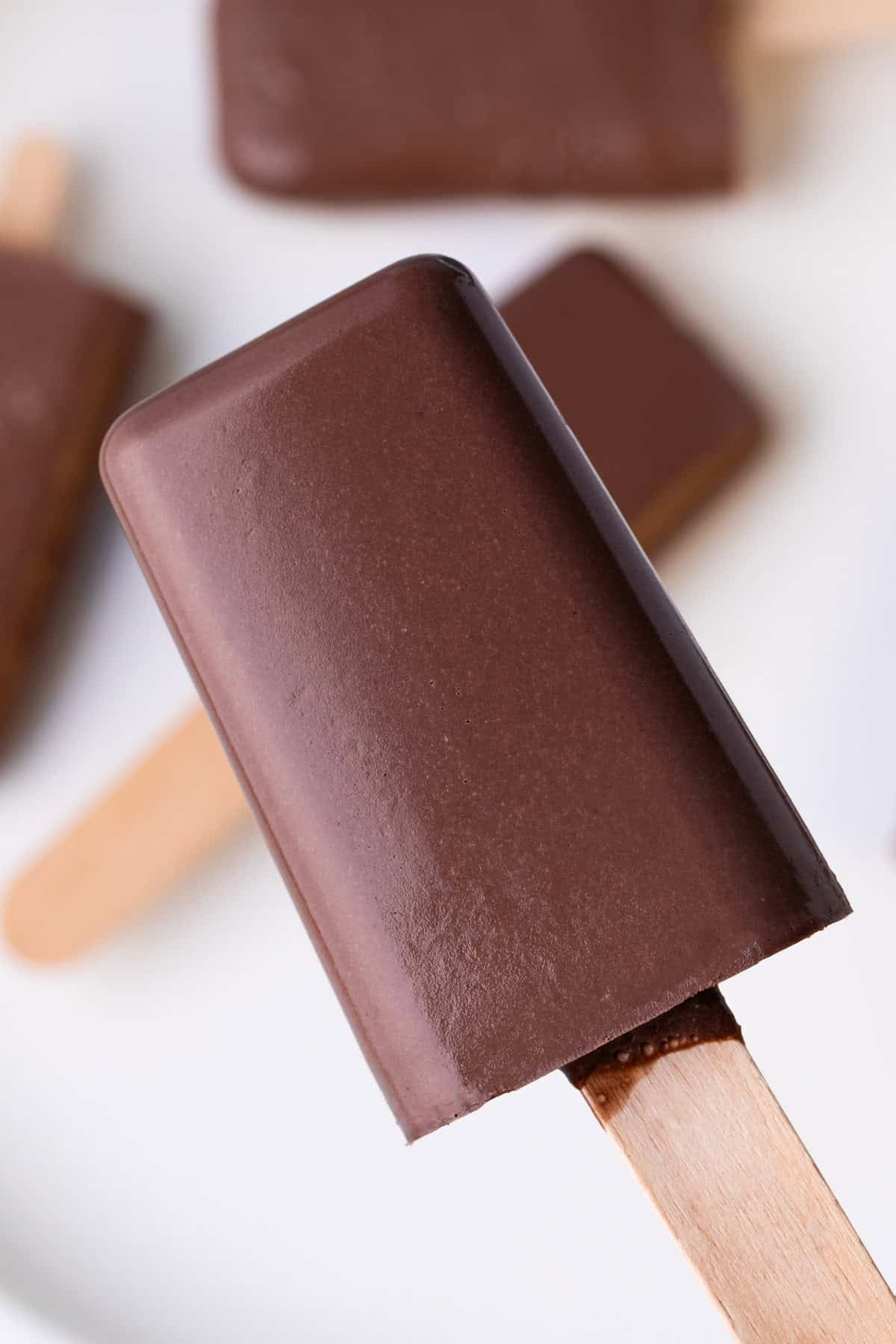Hand holding a thick and creamy chocolate popsicle on a wooden stick.