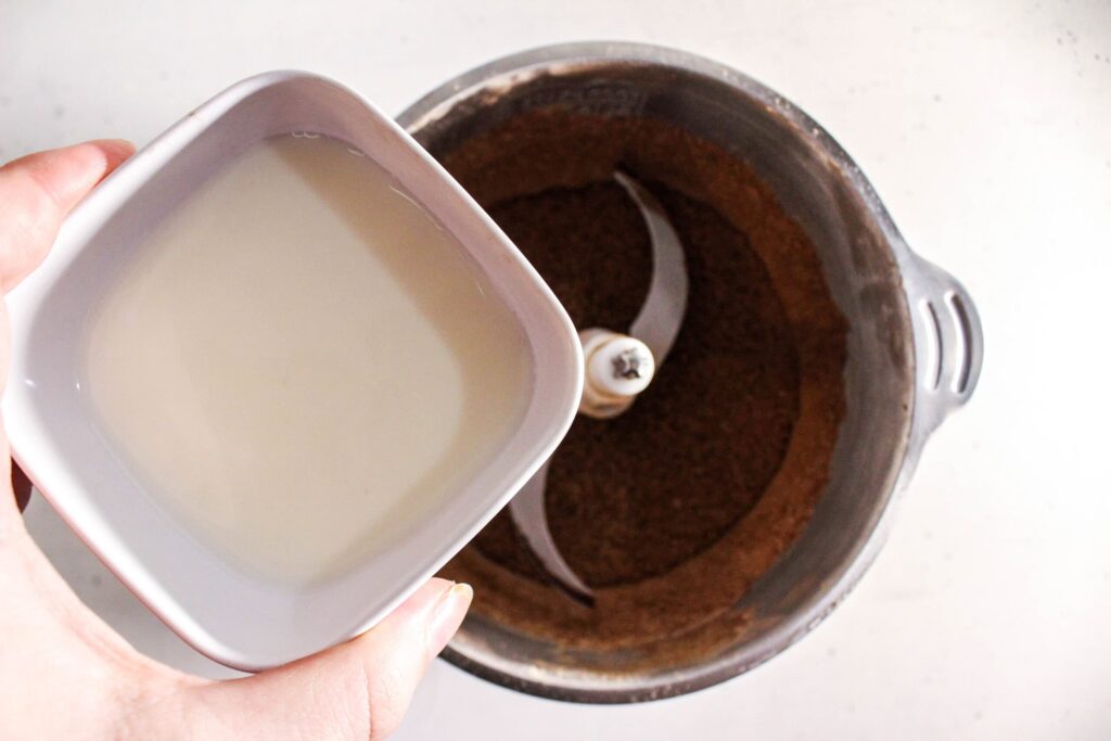 Milk being added to chocolate protein brownie batter in a food processor bowl