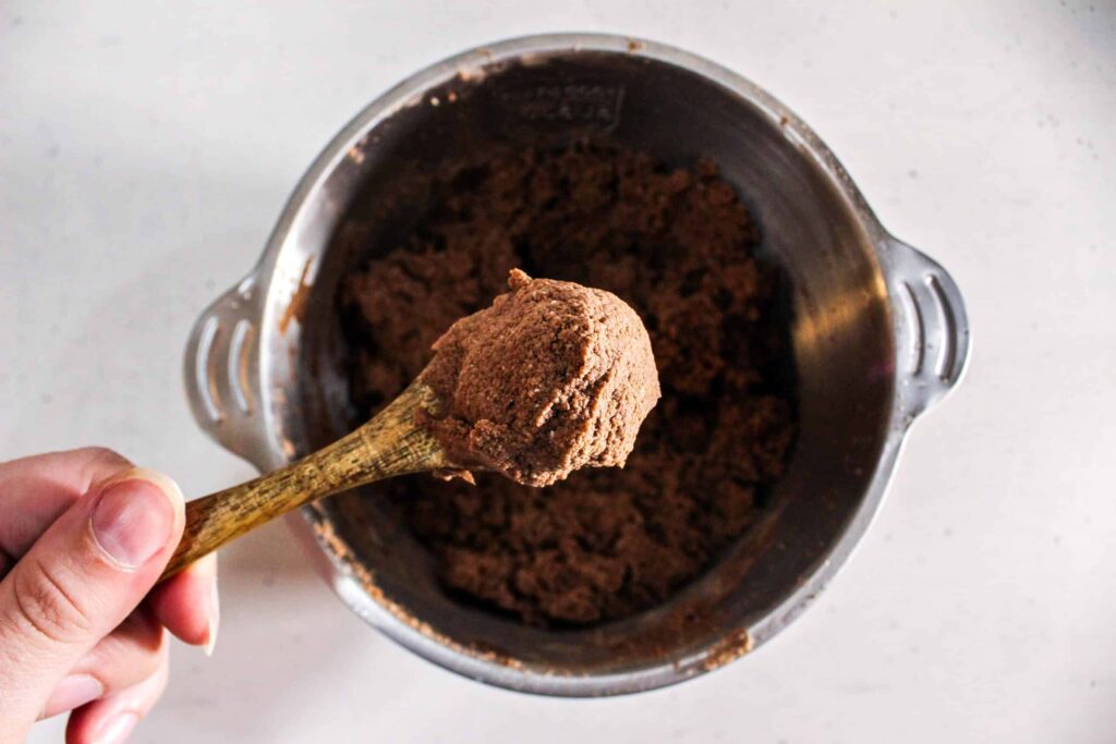 Close-up of a hand holding a spoon full of rich, thick chocolate brownie batter