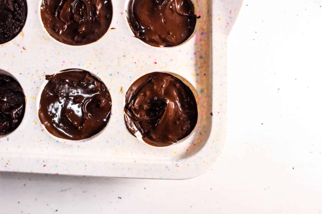 Melted chocolate being poured over brownie bites in a silicone muffin tray