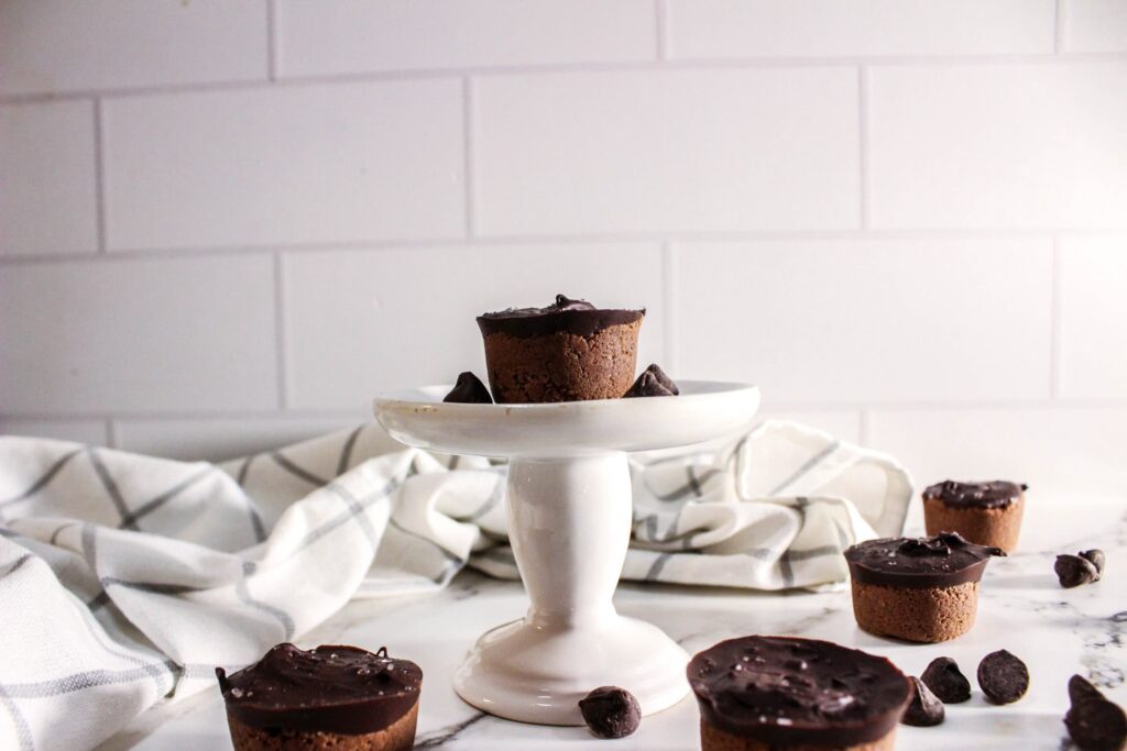 brownie bites topped with chocolate on a white cake stand with chocolate chips scattered around