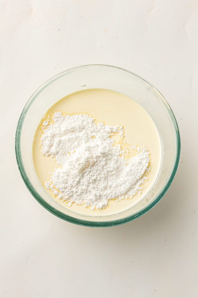 Adding flour into a bowl of wet ingredients.