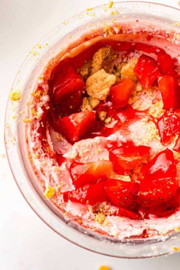 Rich and creamy strawberry ice cream topped with fresh fruit pieces and golden crumbs, slightly melting in a bowl.
